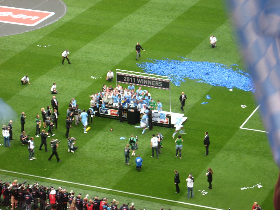 Manchester City players celebrating with the FA Cup trophy on the pitch at Wembley