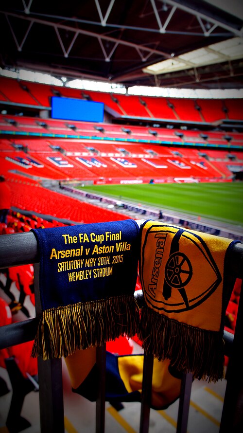 A scarf embroidered with 'The FA Cup Final Arsenal v Aston Villa Saturday May 30th 2015 Wembley Stadium' draped over a railing, with Wembley's red seats behind