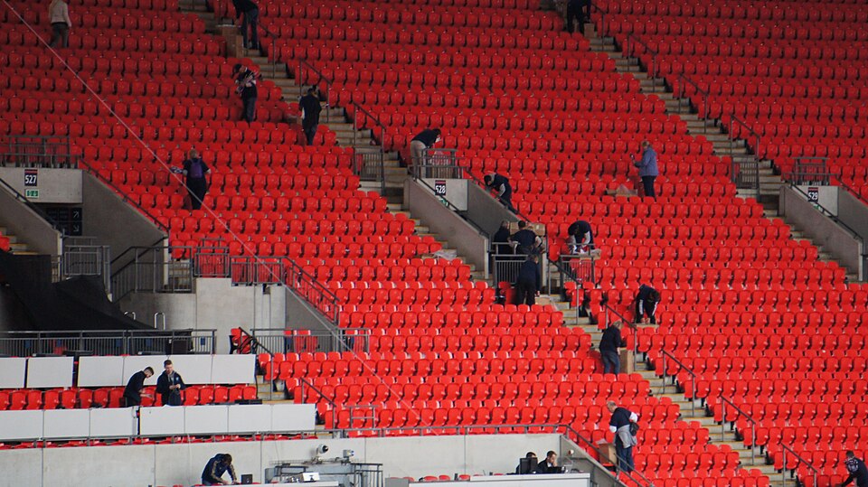 Rows of empty red seats at Wembley with a handful of people scattered through the stands