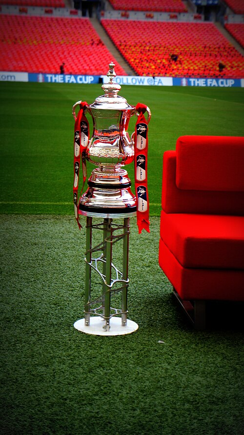 The FA Cup trophy on its plinth at the side of the Wembley pitch, with the stadium seats behind
